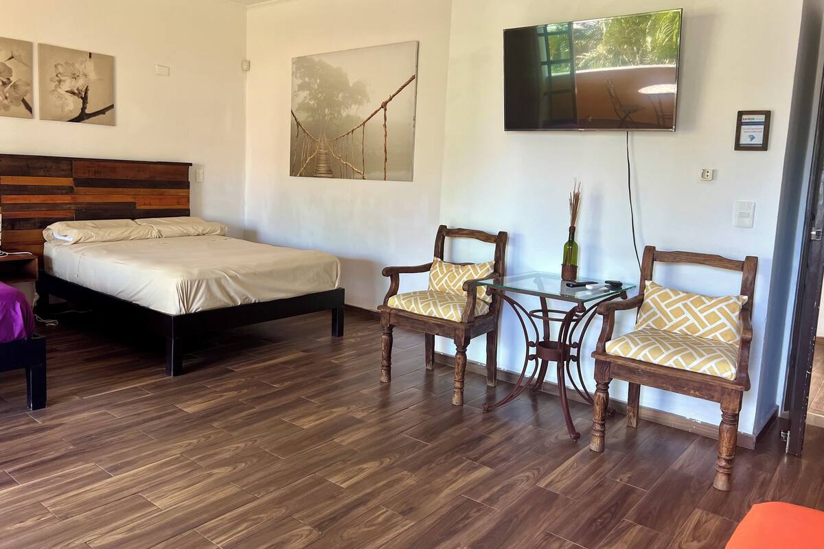 A hotel room with a bed, two chairs, a small table, and a TV on the wall.