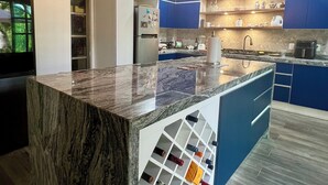 A modern kitchen with a marble island, blue cabinets, and a wine rack. - Cancun - Soho (Cancun)