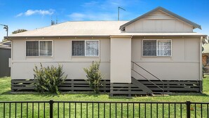A single-story mobile home with a pitched roof, two windows with curtains, a small porch area, and a staircase leading to the entrance.