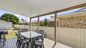 A covered patio with a table and chairs, a grill, and a fenced backyard.