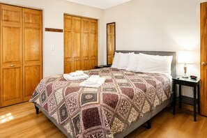 A hotel room with a large bed, a nightstand, a lamp, and wooden wardrobes. - Cooperstown Baseball Rentals  - Elm-Triple Play #1 (Oneonta)