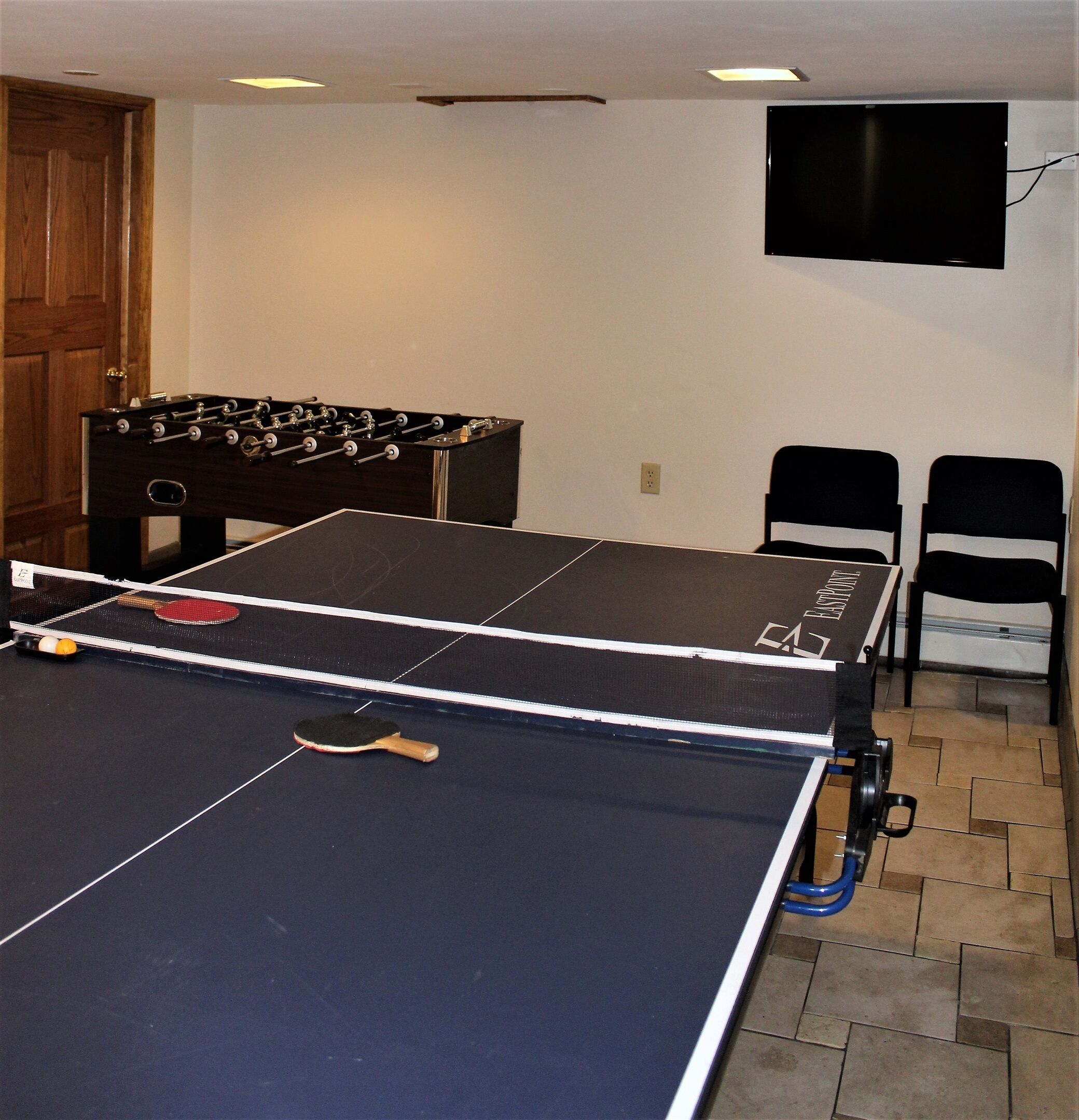 A ping pong table with a net, a foosball table, and two chairs.