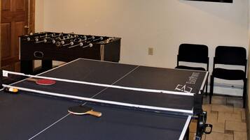 A ping pong table with a net, a foosball table, and two chairs.