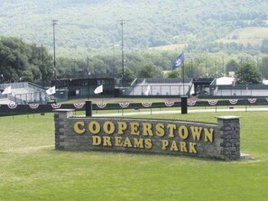 Letrero de Cooperstown Dreams Park sobre una base de piedra, con un campo de césped al fondo.