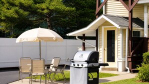 Eine Terrasse im Freien mit Grill, Stühlen und Sonnenschirm.