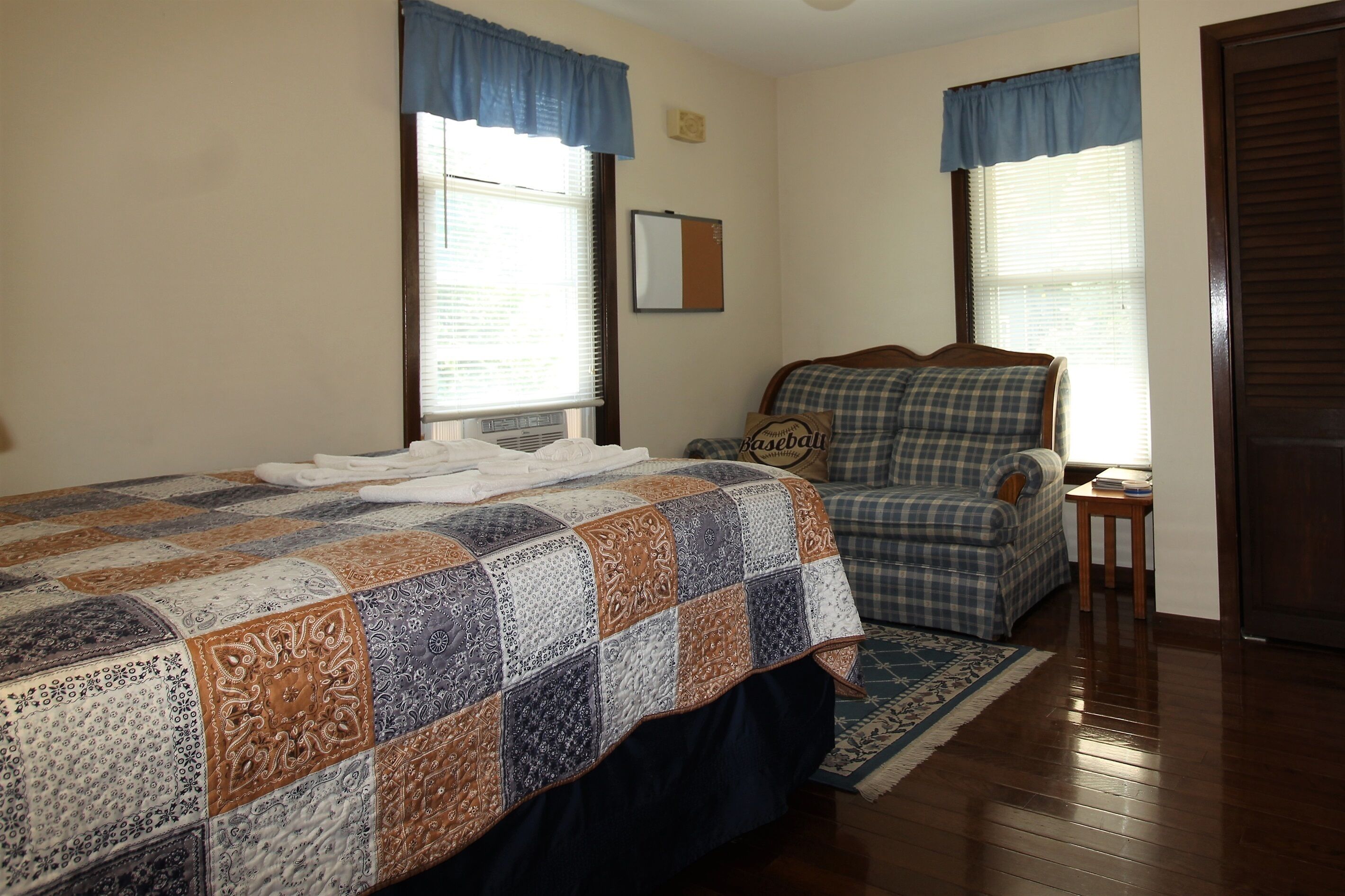 A bedroom with a large bed, a chair, a small table, and a window with blinds.
