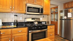 A kitchen with wooden cabinets, a stainless steel stove, a microwave, and a refrigerator. - Cooperstown Baseball Rentals - Elm-Triple Play #2R (Oneonta)
