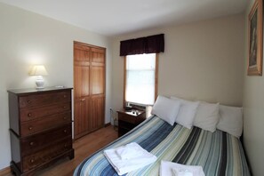 A bedroom with a bed, a dresser, a window with blinds, and a door. - Cooperstown Baseball Rentals - Elm-Triple Play #2R (Oneonta)