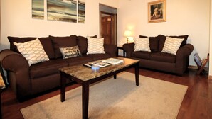 A living room with two brown sofas, a wooden coffee table, and a rug. - Cooperstown Baseball Rentals - Elm-Triple Play #2R (Oneonta)