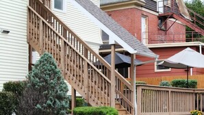 A residential building with a wooden staircase leading to a porch, surrounded by stone walls and greenery. - Cooperstown Baseball Rentals - Elm-Triple Play #2R (Oneonta)