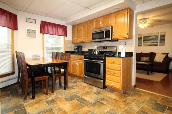 A kitchen with wooden cabinets, a microwave, stove, and a dining table with chairs. - Cooperstown Baseball Rentals - Elm-Triple Play #2R (Oneonta)