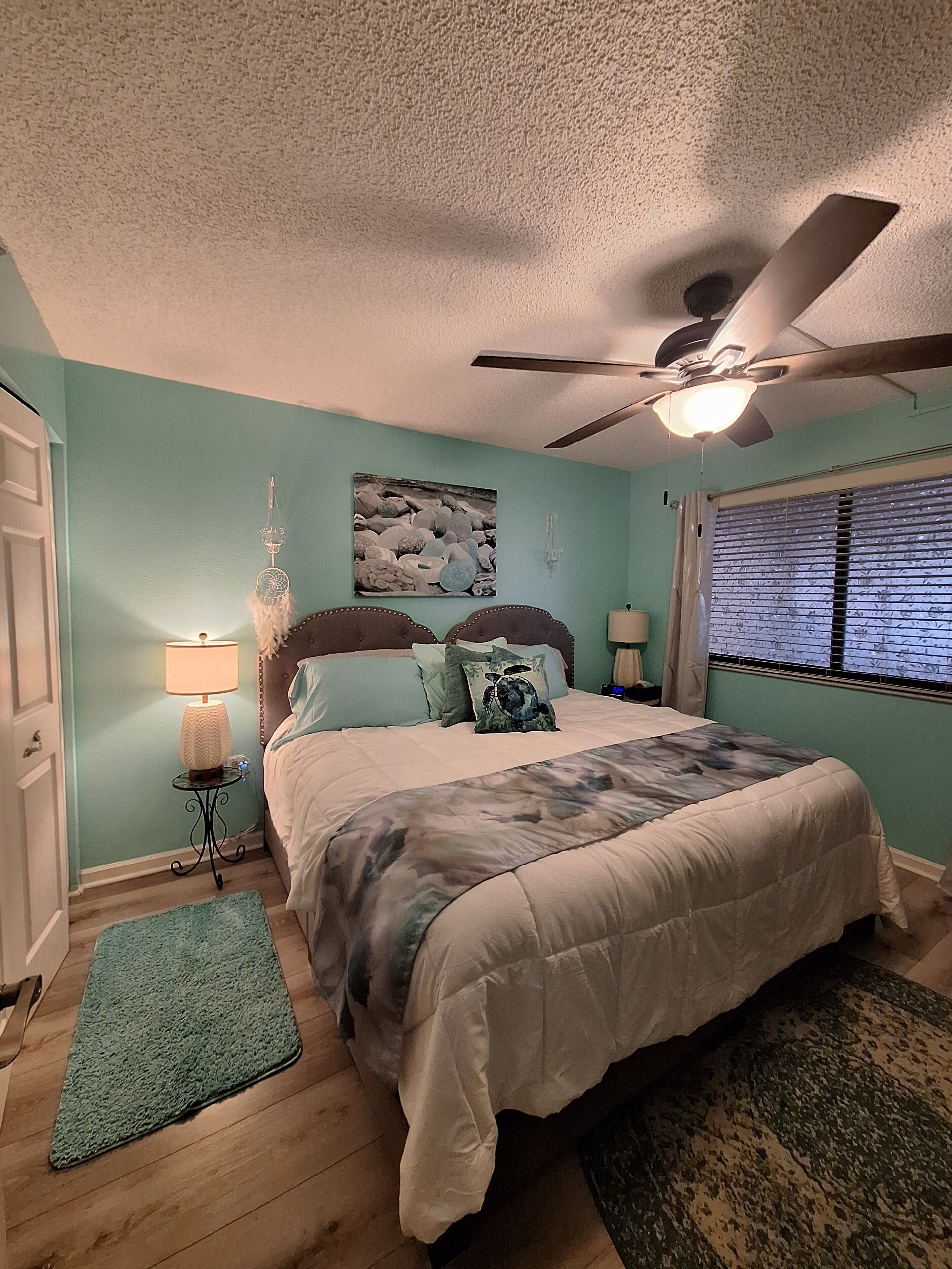 A bedroom with a bed, a ceiling fan, a window with blinds, and a dreamcatcher on the wall.