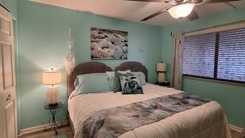 A bedroom with a bed, a ceiling fan, a window with blinds, and a dreamcatcher on the wall.