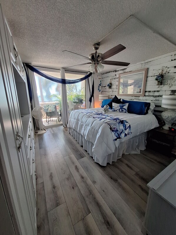 A bedroom with a large bed, a ceiling fan, and a view of the outdoors.