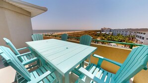 A balcony with a table and chairs, overlooking a beach and a resort area. - Charming Top-Floor Condo w/ Ocean Views, Pool Access (Tybee Island)