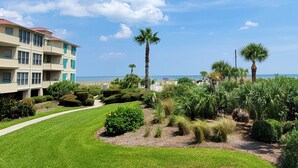 A hotel with a well-maintained lawn, palm trees, and a view of the ocean. - Charming Top-Floor Condo w/ Ocean Views, Pool Access (Tybee Island)