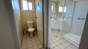 A bathroom with a toilet, a shower, and a sink. - Central 2BR unit with garage, walk to beach, river, shops & cafes in Evans Head. (Evans Head)