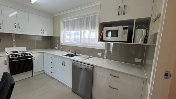 A compact kitchen with white cabinets, a stainless steel sink, a microwave, a stove, and a dishwasher. - Central 2BR unit with garage, walk to beach, river, shops & cafes in Evans Head. (Evans Head)