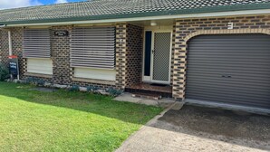 A two-story building with a brick facade, a garage door, and a sign indicating 'Holiday Letting.' - Central 2BR unit with garage, walk to beach, river, shops & cafes in Evans Head. (Evans Head)
