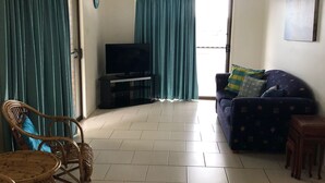 A living room with a sofa, a television, a wicker chair, and a small table. - 2/36 Sunderland Street, Evans Head (Evans Head)