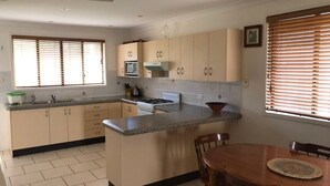 A kitchen with beige cabinets, a stove, a sink, and a dining area with a table and chairs. - 2/36 Sunderland Street, Evans Head (Evans Head)