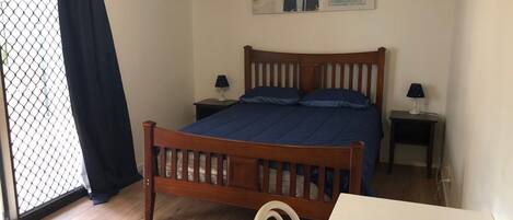 Een slaapkamer met een houten bed, twee nachtkastjes met lampen, een klein bureau, een stoel, een raam met gordijn en een decoratie aan de muur.