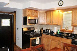 A compact kitchen with wooden cabinets, a black stove, a microwave, and a sink. - Cooperstown Baseball Rentals - Columbia House (Oneonta)