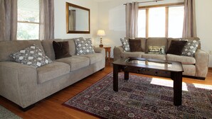 A living room with two sofas, a coffee table, a patterned rug, and a ceiling fan. - Cooperstown Baseball Rentals - Columbia House (Oneonta)