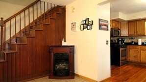 A home interior with a wooden staircase, a fireplace, a kitchen with wooden cabinets, and a tiled floor. - Cooperstown Baseball Rentals - Columbia House (Oneonta)