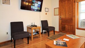 A room with two chairs, a wooden table with a book and a remote, and a TV displaying streaming services.