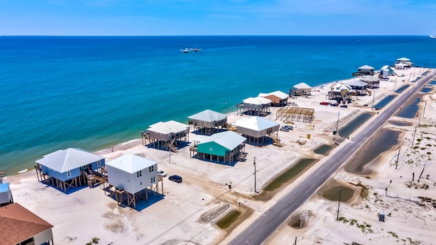 An aerial view of a coastal area with multiple buildings on stilts, a road, and a beach.