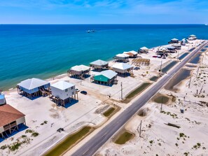 An aerial view of a coastal area with multiple buildings on stilts, a road, and a beach. - Gulf-side Beach house, great layout on beach and close walk to water! - Beach Br (Dauphin Island)
