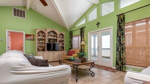 A living room with a sofa, a coffee table, and a TV. There is a bookshelf with decorative items and a window with curtains.
