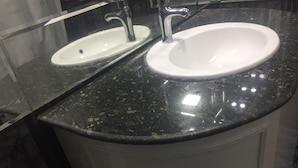 Een badkamer met twee wastafels, waarvan één met een kraan en de ander met een afvoer. Het aanrecht is zwart met stipjes, en de wastafel is wit.