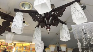 Een kroonluchter met meerdere witte lampenkappen, versierd met zwarte patronen, hangend aan een donker metalen frame.