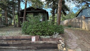 Una cabaña rústica con terraza de madera, rodeada de abundante vegetación y un sendero de piedra.
