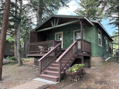A cabin with a wooden deck, a staircase, and a wheelbarrow with flowers.
