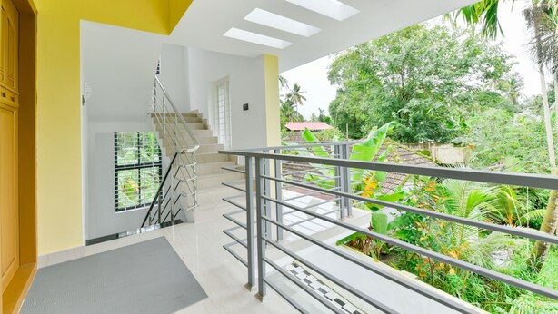 Un interior moderno con una escalera que conduce a un balcón con vistas a un jardín exuberante.