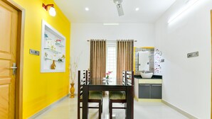 Un comedor con mesa y sillas de vidrio, una cocina con pileta y encimera, y una pared de acento amarilla.