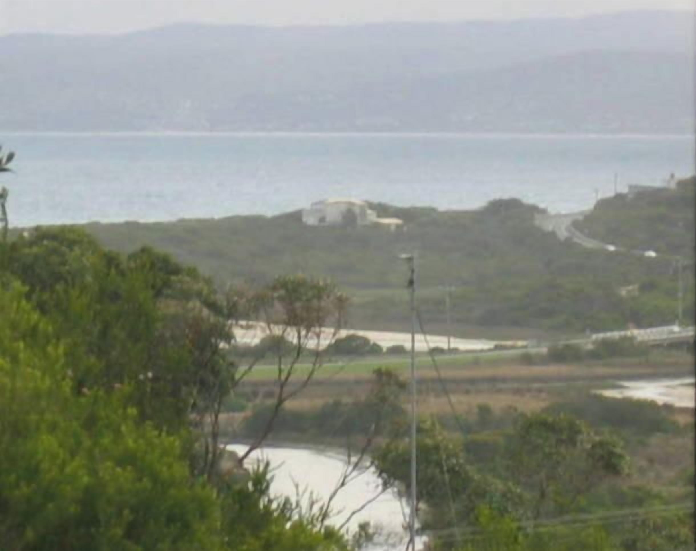 Eine Küstenlandschaft mit Wasser, Vegetation und einem Gebäude in der Ferne.