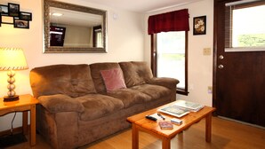 A living room with a brown sofa, a wooden coffee table, a lamp, a mirror, and a door with a window. - Cooperstown Baseball Rentals - 1st Baseman (Oneonta)