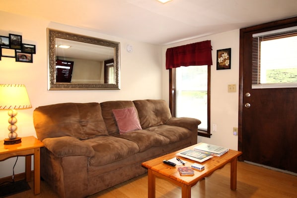 A living room with a brown sofa, a wooden coffee table, a lamp, a mirror, and a door with a window.