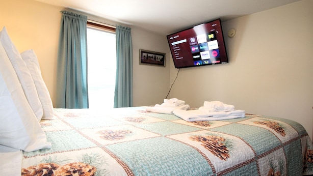 A hotel room with a bed, a flat-screen TV mounted on the wall, and a window with curtains. - Cooperstown Baseball Rentals - 1st Baseman (Oneonta)