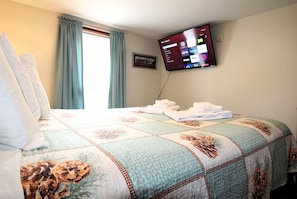 A hotel room with a bed, a flat-screen TV mounted on the wall, and a window with curtains.