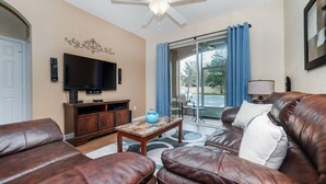 A living room with a brown leather sofa, a TV, a wooden cabinet, and a coffee table.