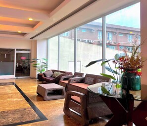 A modern lobby with a large window, wicker furniture, and a potted plant.