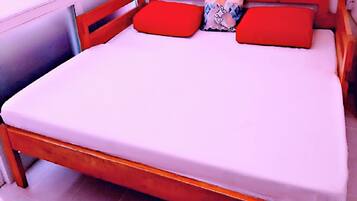 A bed with a wooden frame, red pillows, and a white mattress in a room with white walls and tiled flooring.