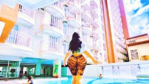 A poolside area with a person walking, a building with balconies, and a clear sky. - BestLove HideAway 1-BR *Parking, Pool (Tagaytay)