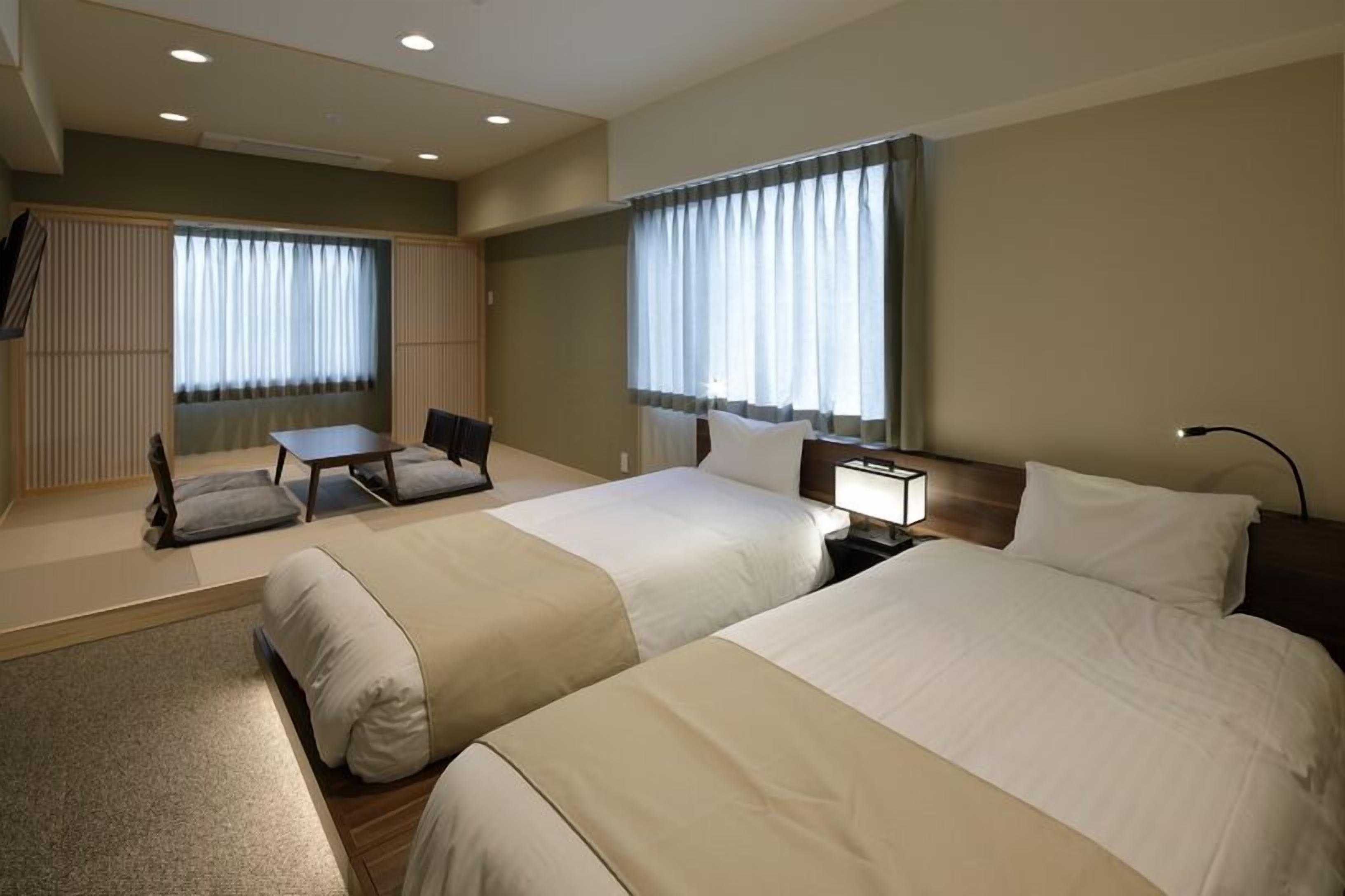 A hotel room with two beds, a desk, a chair, and a TV.