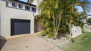A modern two-story house with a garage, a concrete driveway, and a well-maintained garden with palm trees.